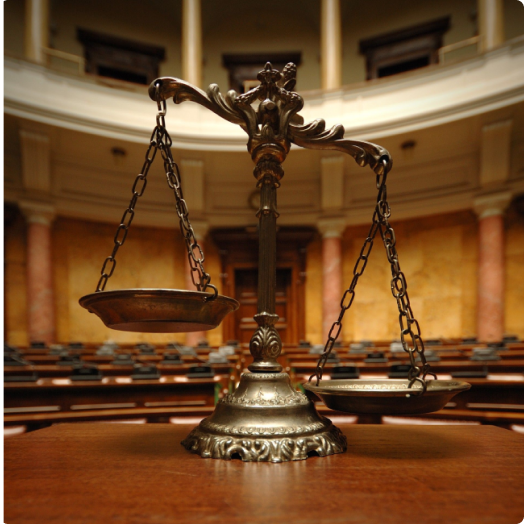 Scales of Justice sitting on a table in an empty legislative chamber or courtroom.