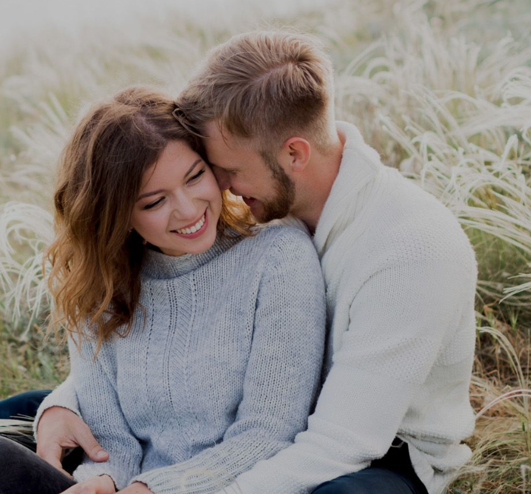 Una pareja feliz comprometida para casarse sentada en un prado.