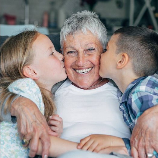Una abuela recibe besos en las mejillas de su nieto y su nieta.