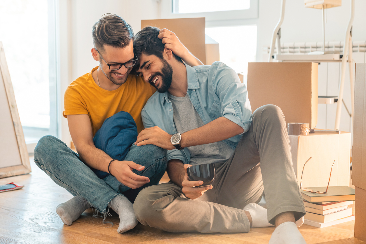 Linda pareja homosexual sentada en el suelo y disfrutando de un nuevo hogar