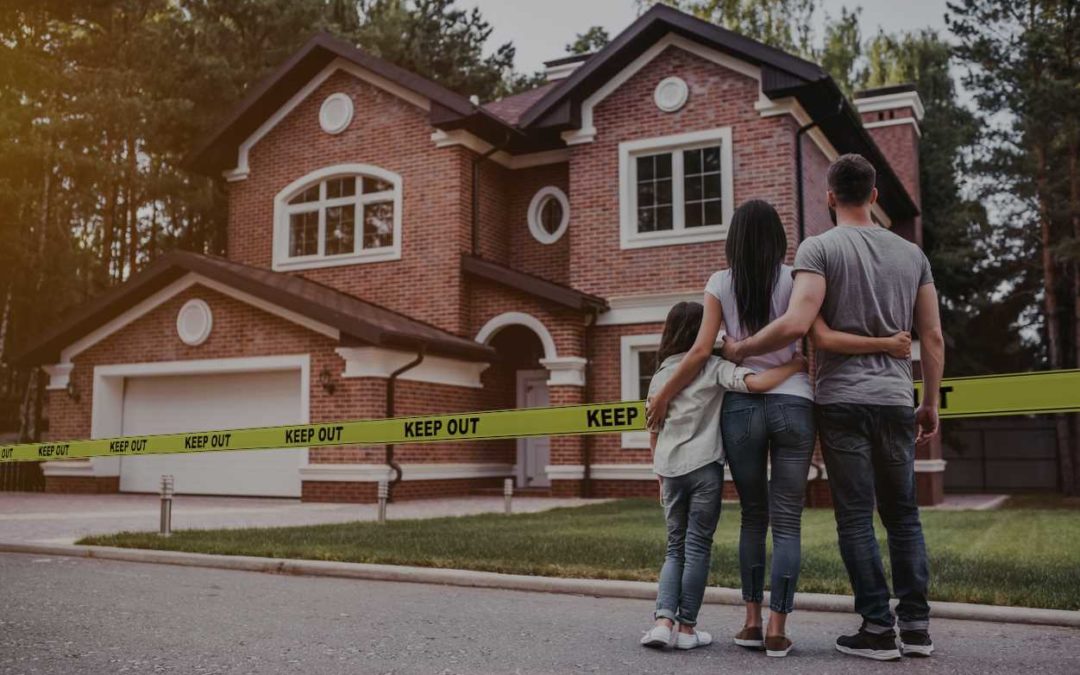 Parents and young daughter embracing while looking at 2-story brick home with Keep Out yellow tape around it