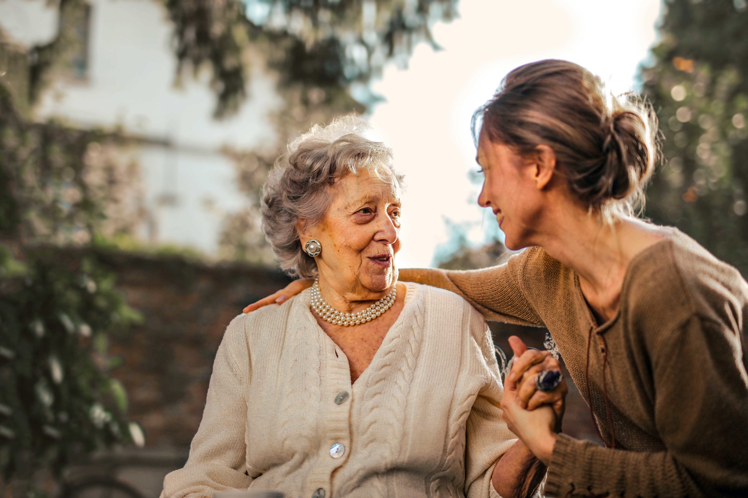 Mujer con su brazo alrededor de su anciana madre mientras está sentada afuera