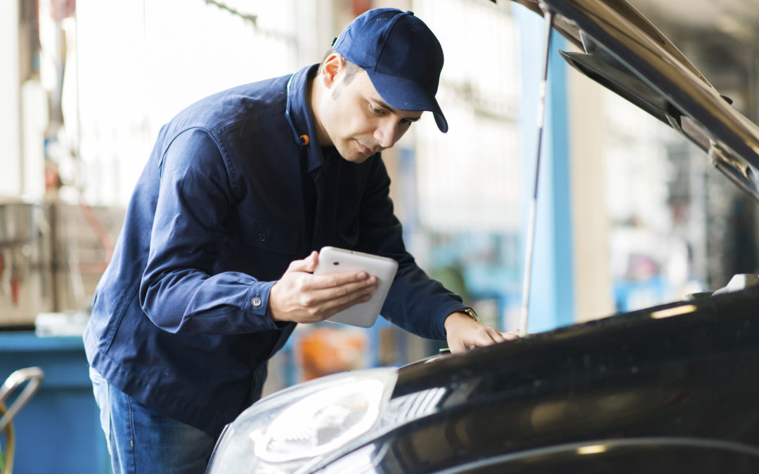 Auto mechanic working on vehicle & looking at data on handheld device