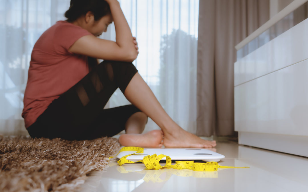 woman upset about her weight sitting on floor next to scale & tape measure