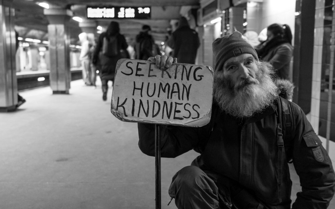 Homeless man in subway holding sign that says Seeking Human Kindness