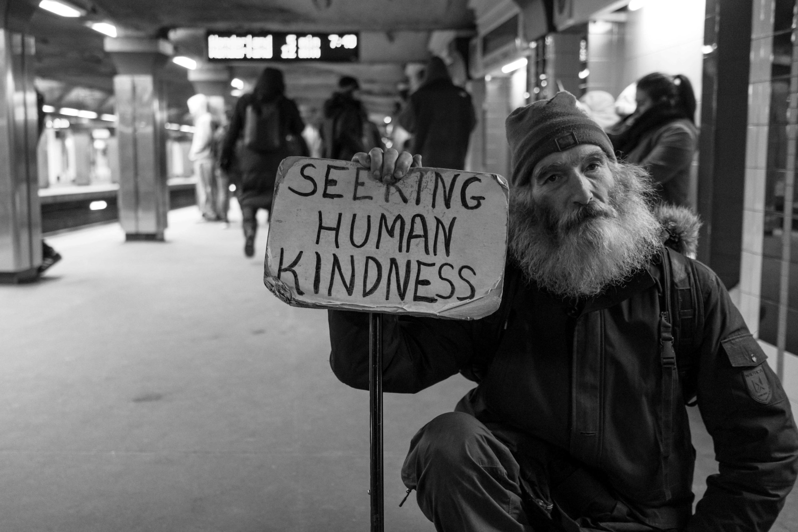 Hombre sin hogar en el metro con un cartel que dice Buscando la bondad humana