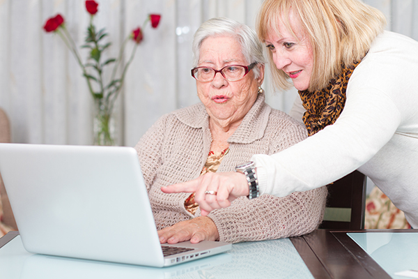 Woman helping an older mature woman use a laptop