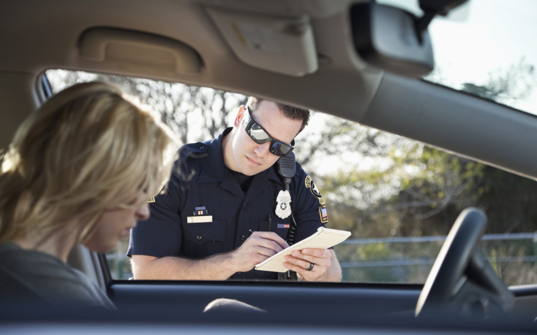 Policía de tránsito mirando en el auto y escribiendo un boleto mientras la mujer conductora está buscando documentos