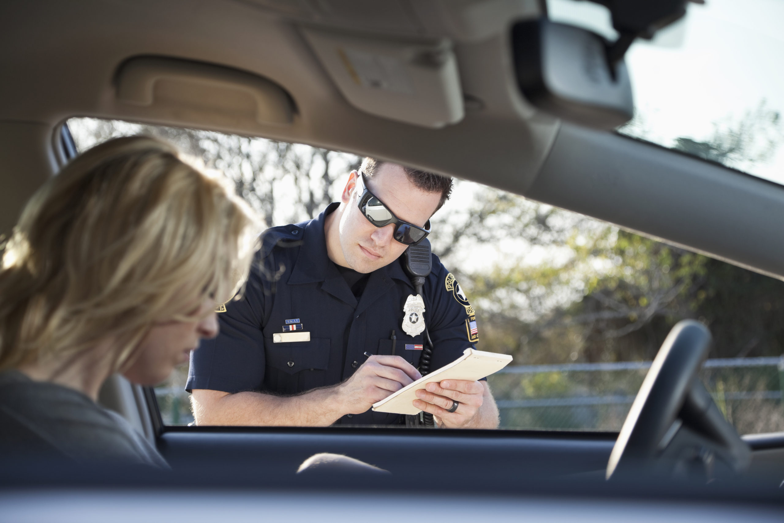 Oficial de policía mirando en el auto y escribiendo una multa mientras la conductora busca documentos