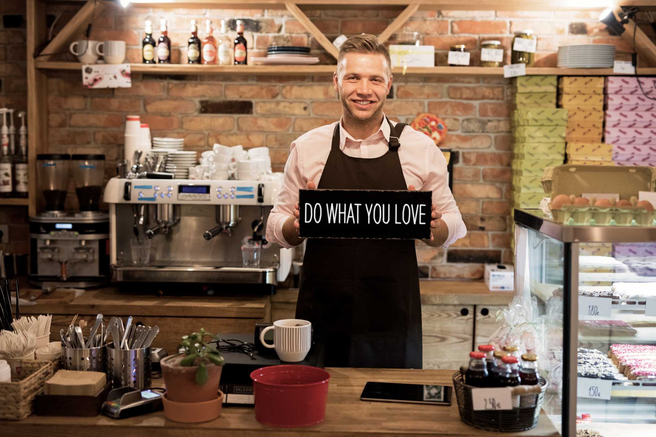 Small business coffee shop owner holding a sign that says, Do What You Love