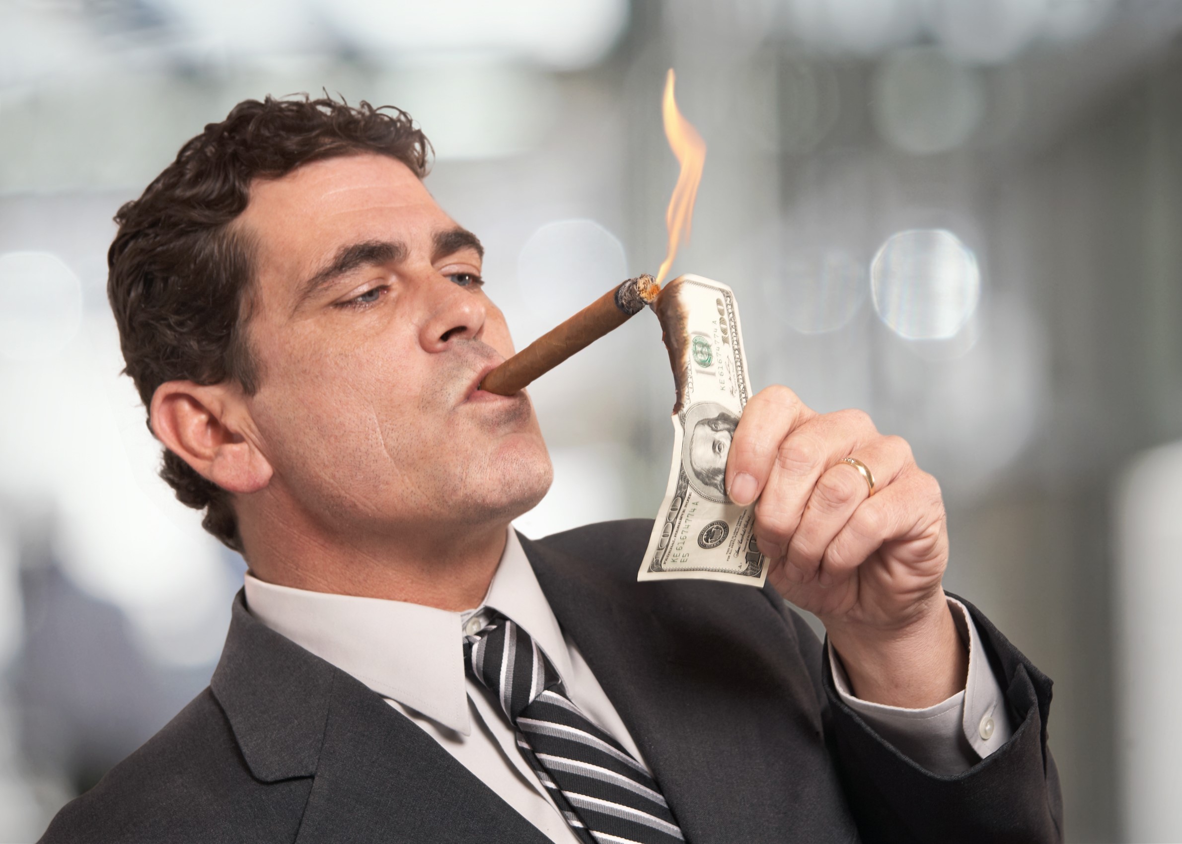 Abogado hombre fumando un cigarro y quemando un billete de cien dólares