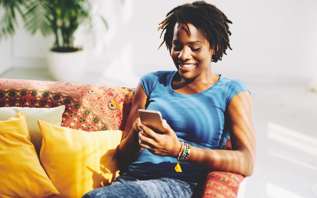Smiling woman sitting on sofa while texting on her smartphone