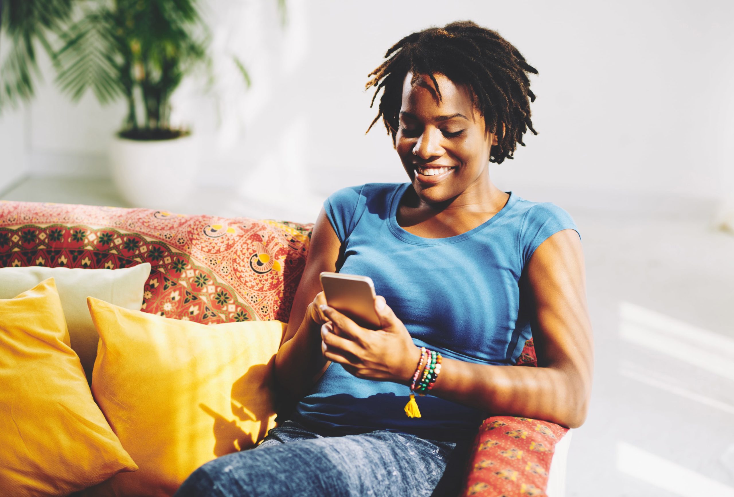 Mujer sonriente sentada en el sofá mientras envía mensajes de texto en su teléfono inteligente