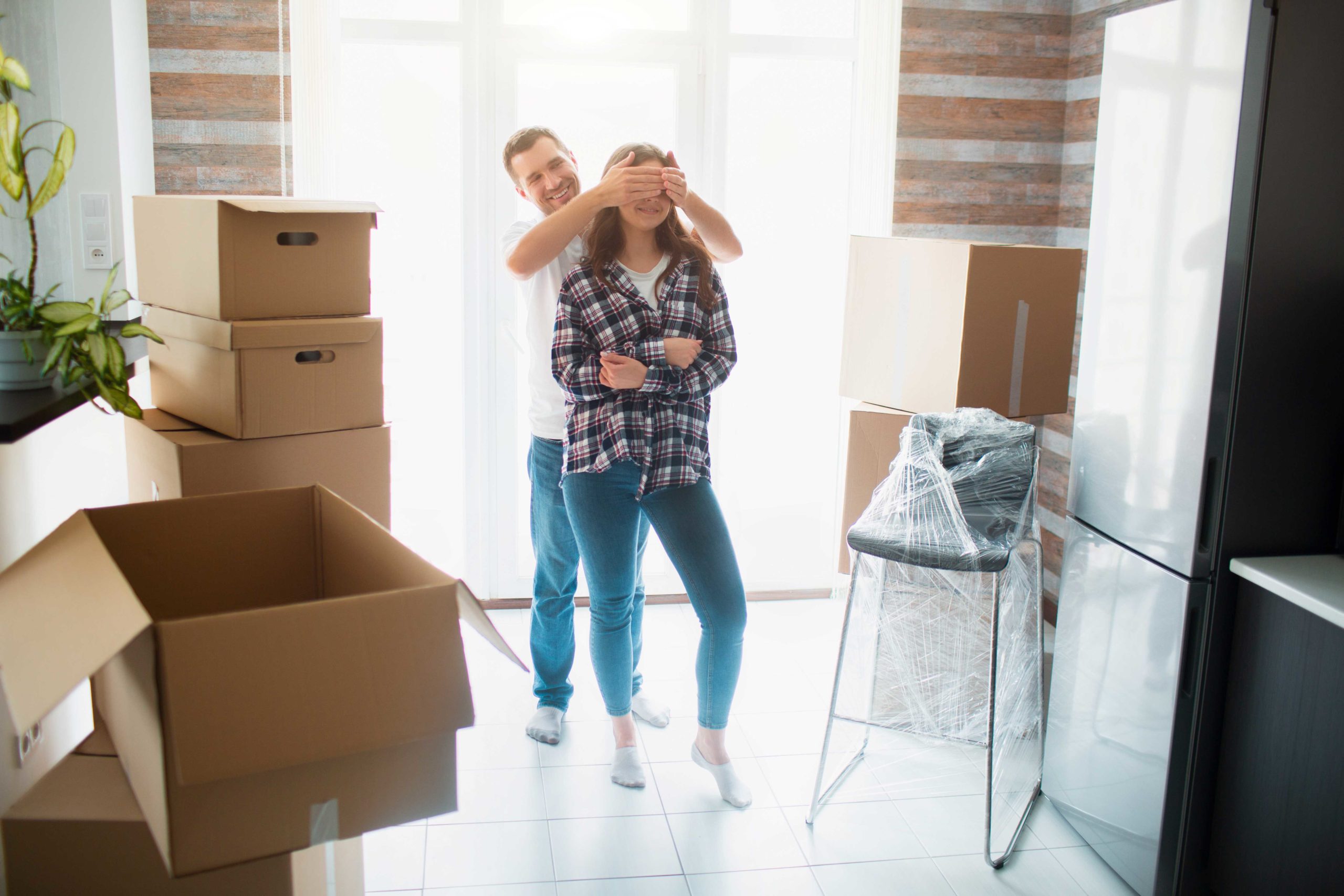 Man holding his hands over eyes on partner as they move into a new home