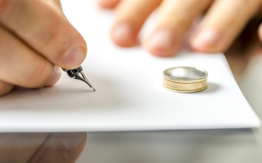Hombre firmando un documento de divorcio junto al anillo de bodas