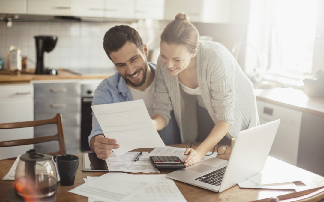Young couple smiling and reviewing financial documents at their kitchen table