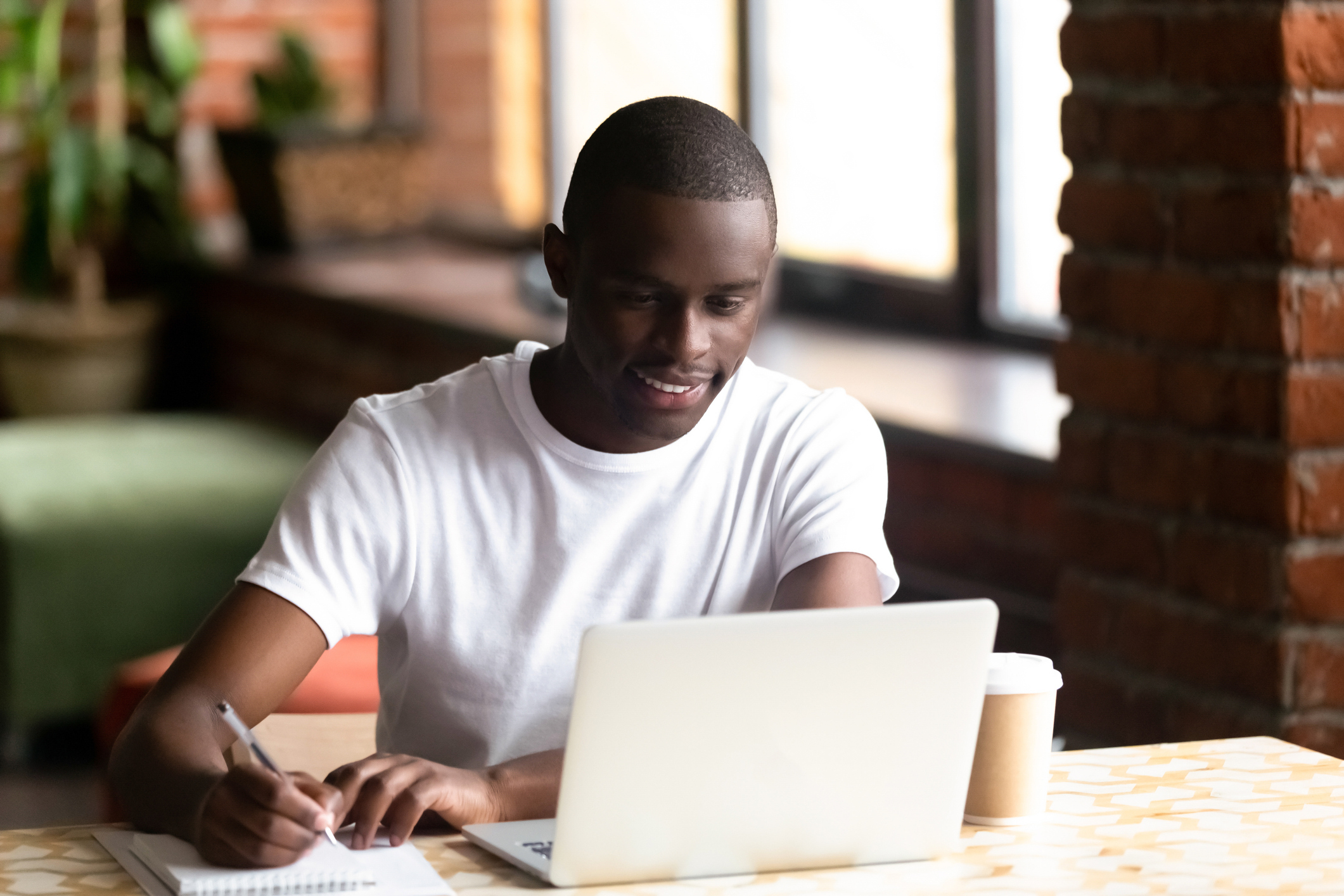 Estudiante universitario estudiando usando su computadora portátil y tomando notas