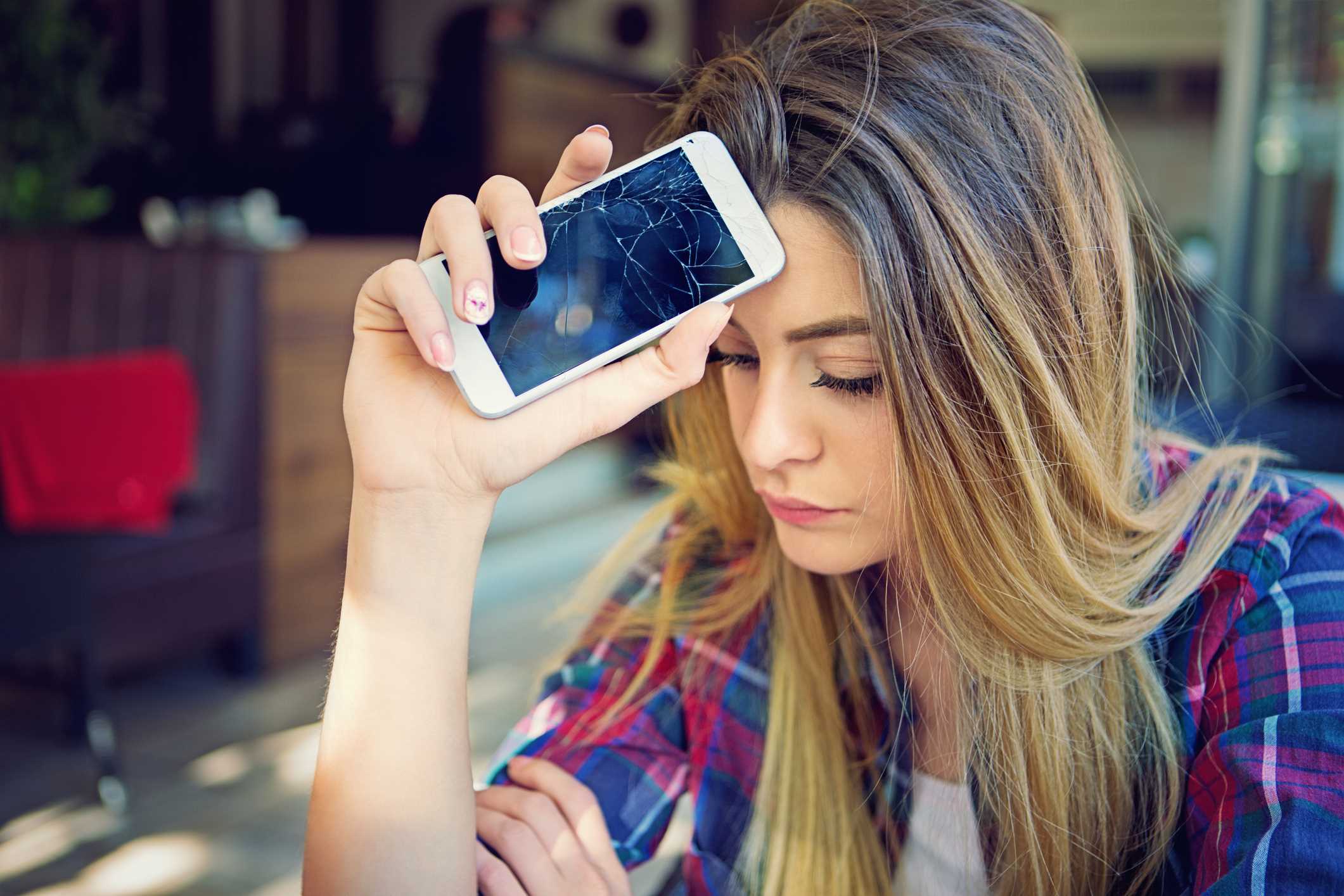 Adolescente angustiado sosteniendo un teléfono inteligente destrozado que no funciona