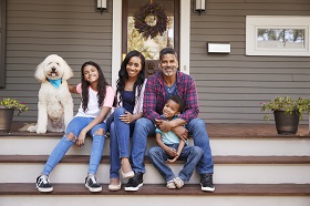 Young family of four sitting on porch with large dog