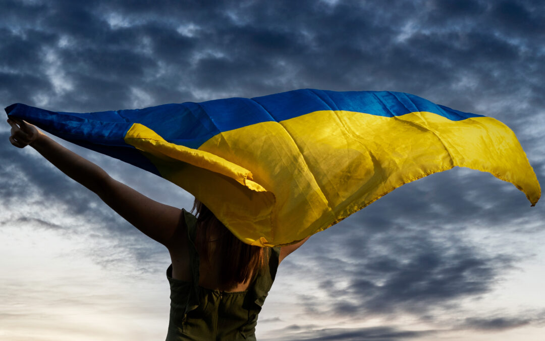 Ukrainian woman proudly holding country's blue and yellow flag outside with clouds in the background