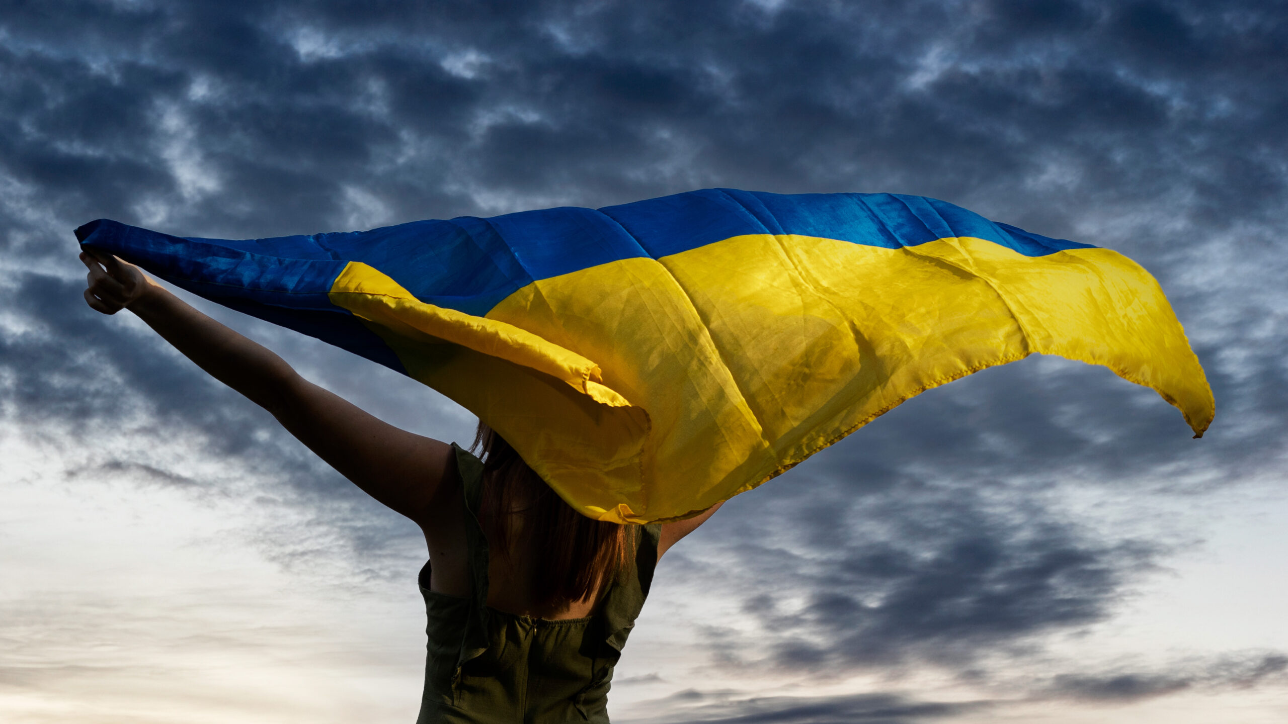 Mujer ucraniana orgullosamente sosteniendo la bandera azul y amarilla del país afuera con nubes en el fondo