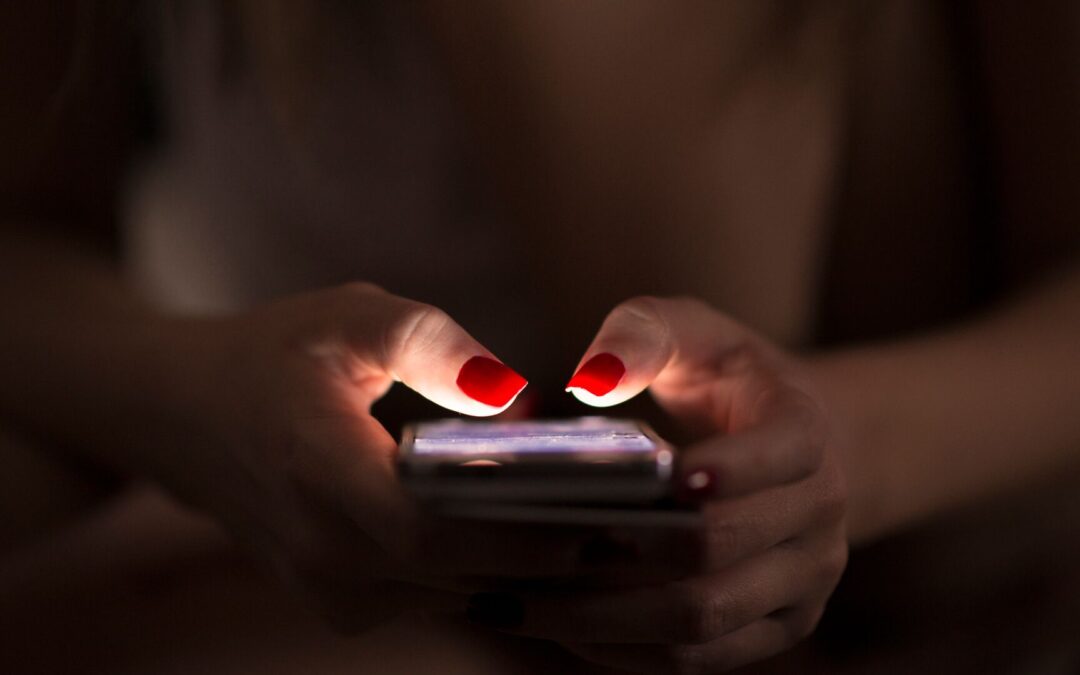 A woman using a cell phone in the dark. Her fingernails are painted bright red.