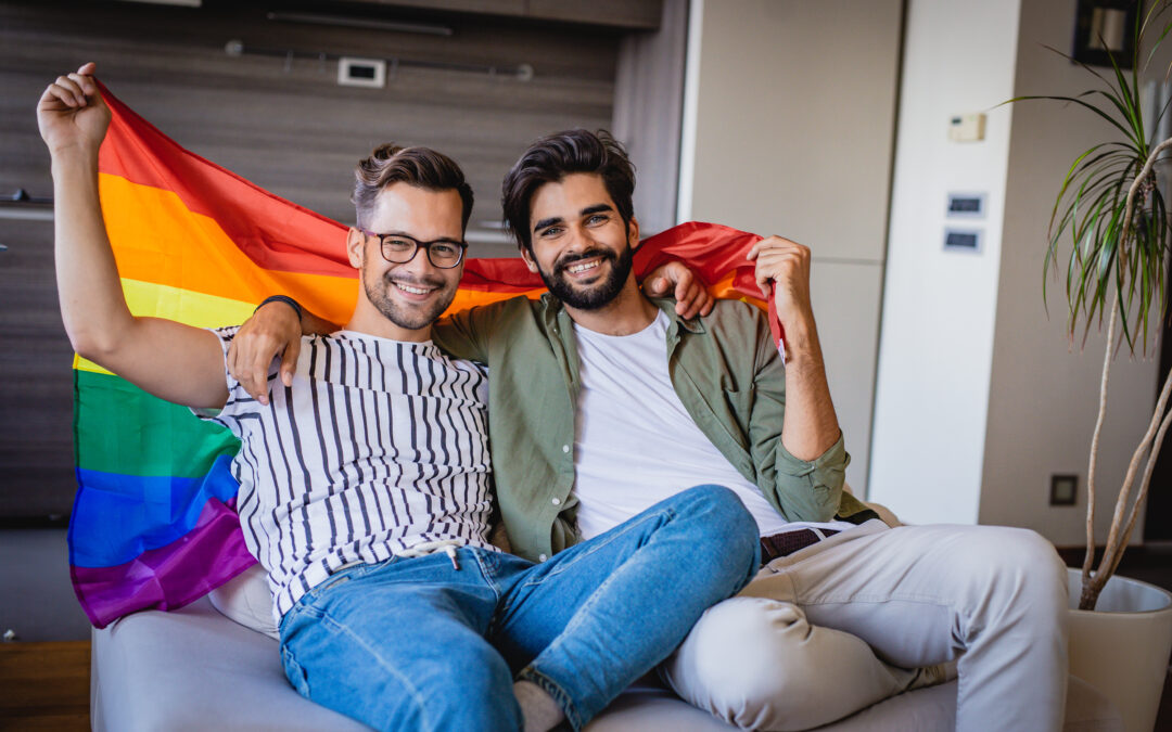 Two people on couch holding a gay pride rainbow flag