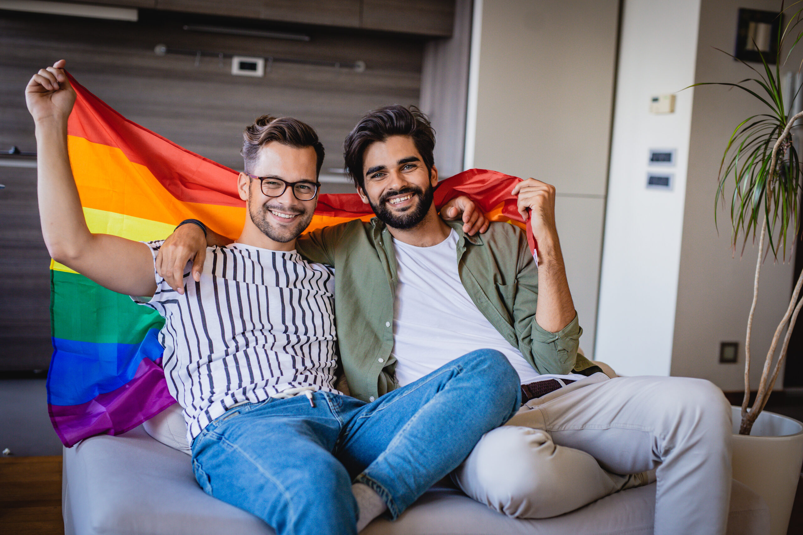 Dos personas en un sofá sosteniendo una bandera del arco iris del orgullo gay
