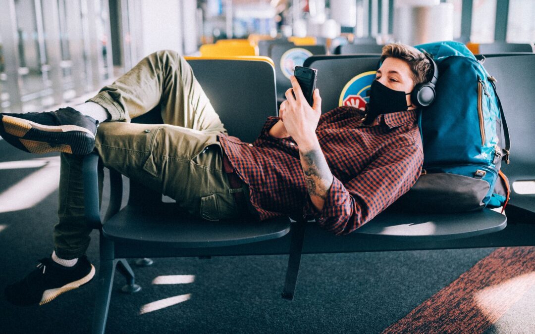 man laying across chairs at an airport as he looks at his smartphone