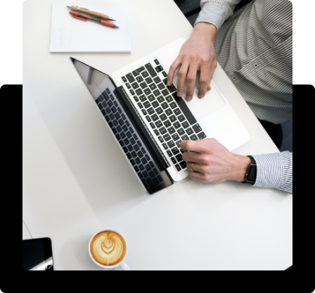 Hombre tecleando en un ordenador portátil. Cerca hay una taza de café.