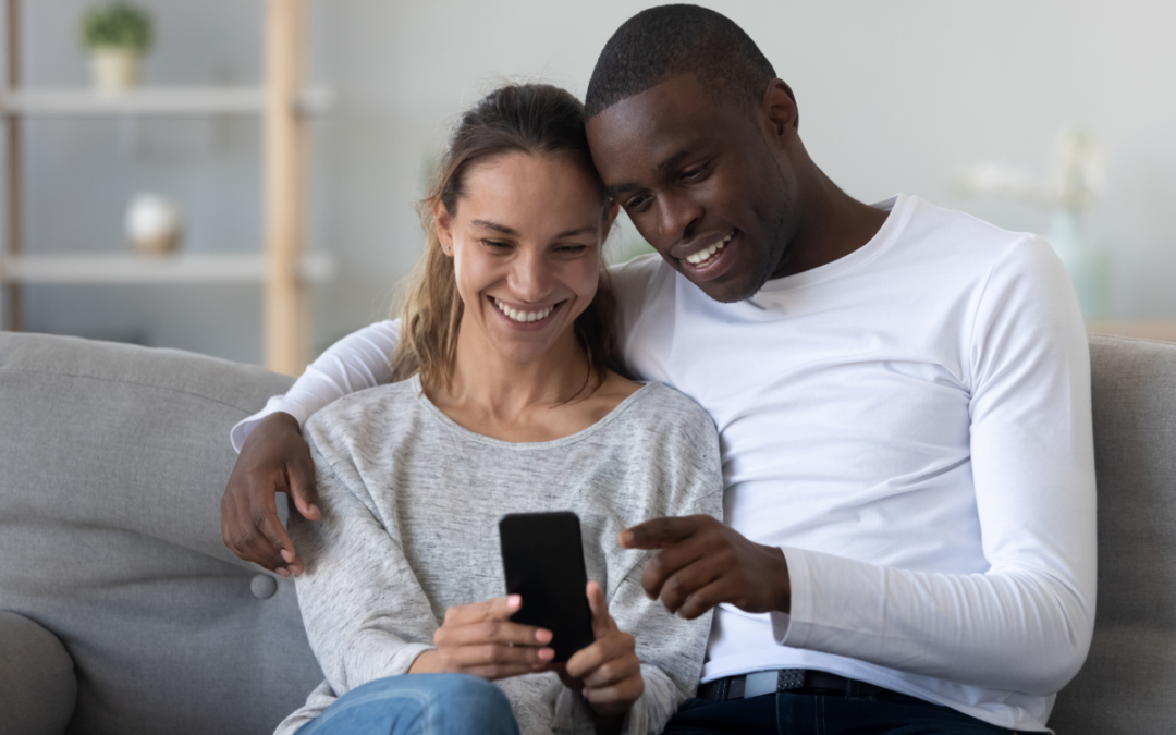 Feliz pareja sentada en un sofá y mirando un acuerdo prenupcial en un teléfono inteligente