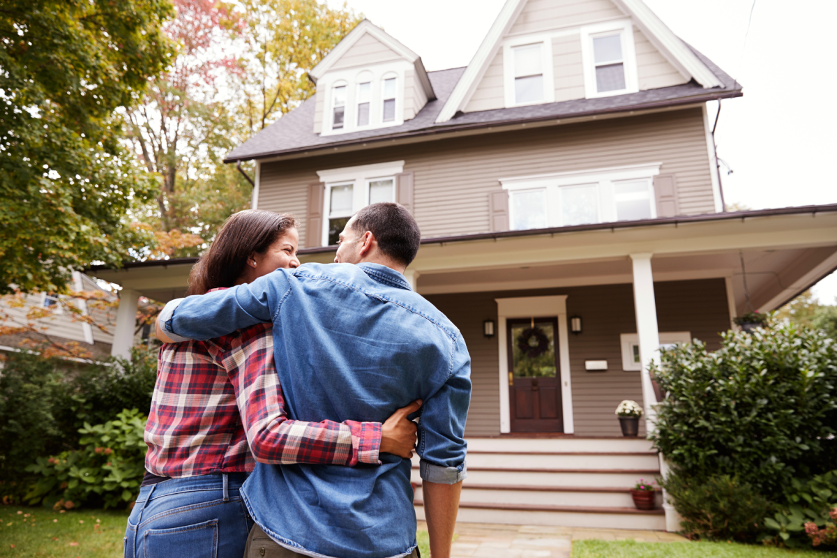 Homeowners in the front yard embracing and looking at their home