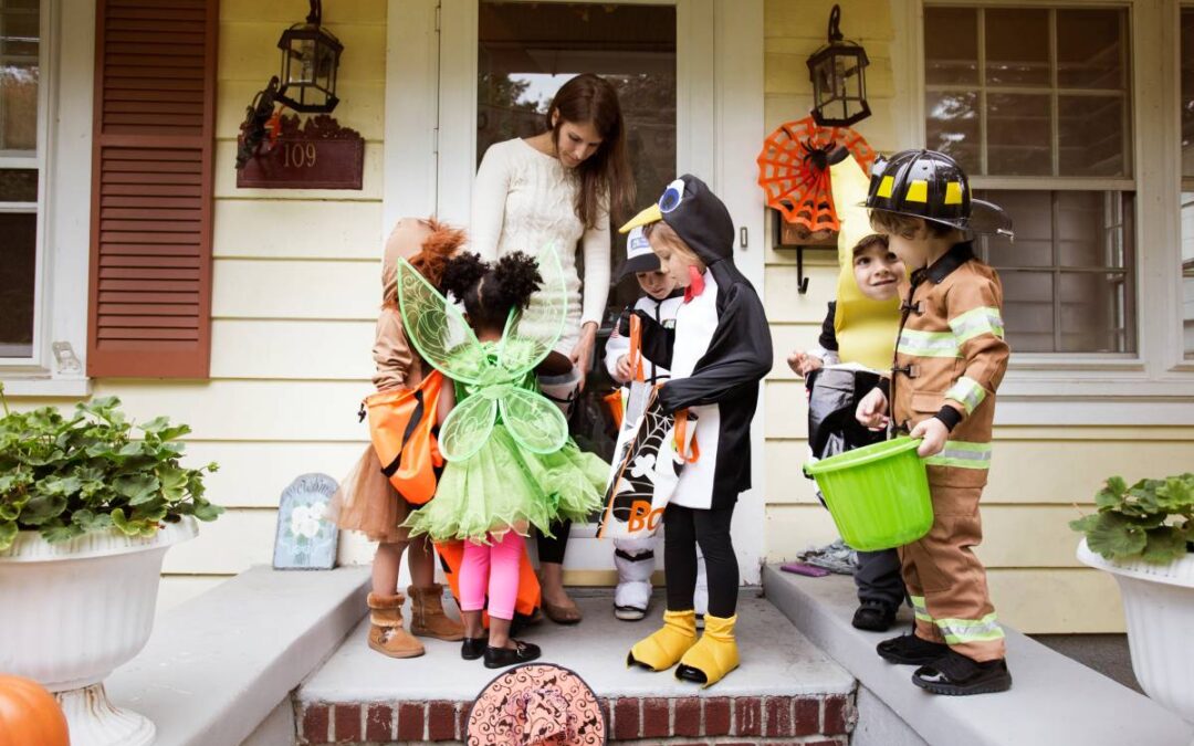 6 kids in Halloween costumes getting candy from a woman on her doorstep.
