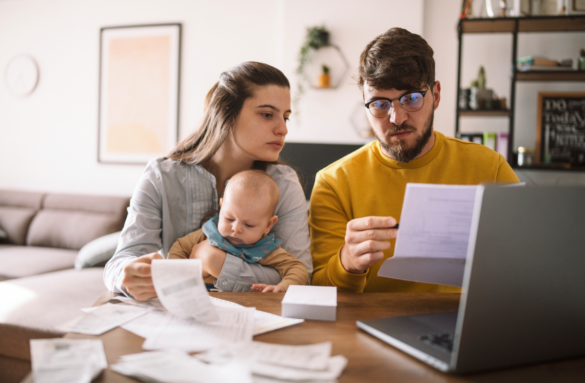 Padres con un bebé pequeño sentados frente a un ordenador portátil y trabajando para presentar un formulario de prórroga de impuestos a Hacienda.