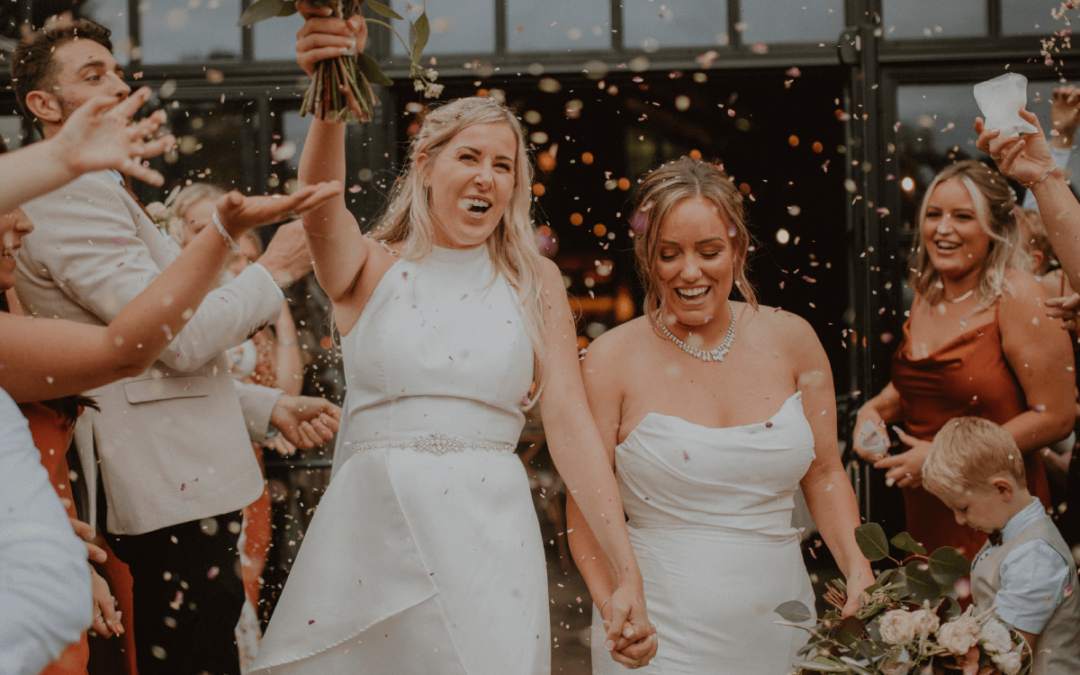 2 novias saliendo de su ceremonia de matrimonio en celebración mientras les arrojan confeti.