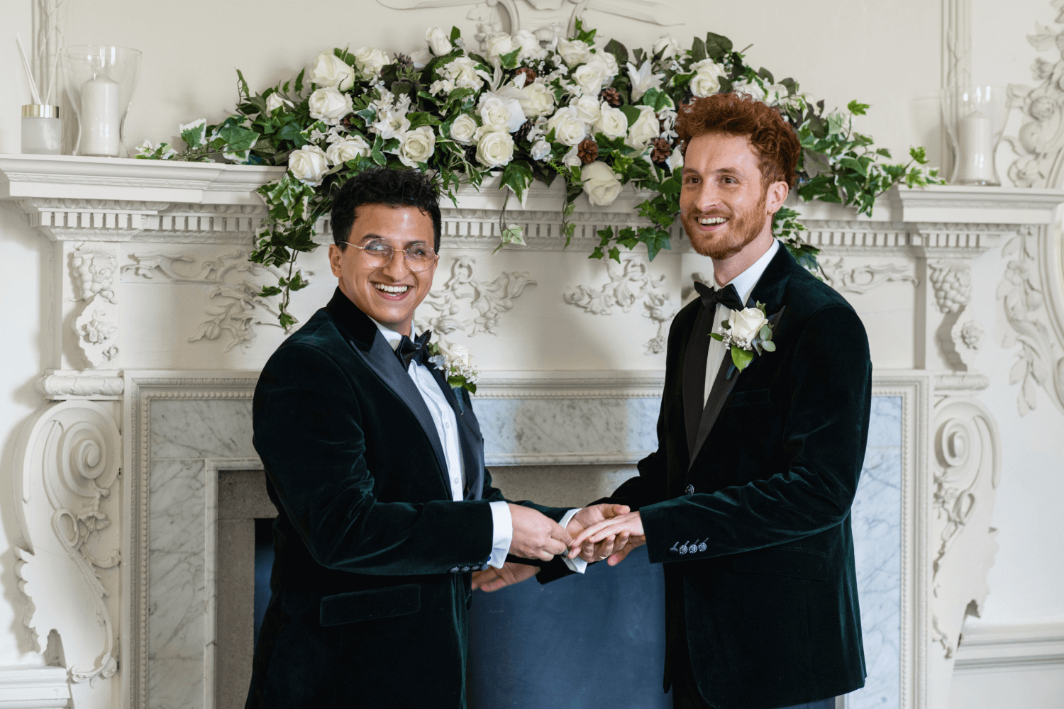 2 grooms smiling as one placing a wedding ring on the other during their gay marriage ceremony.
