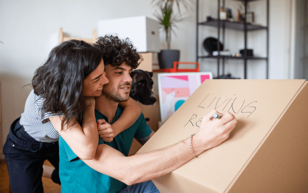 A man labeleling a moving box with Living Room as he girlfriend looks on.