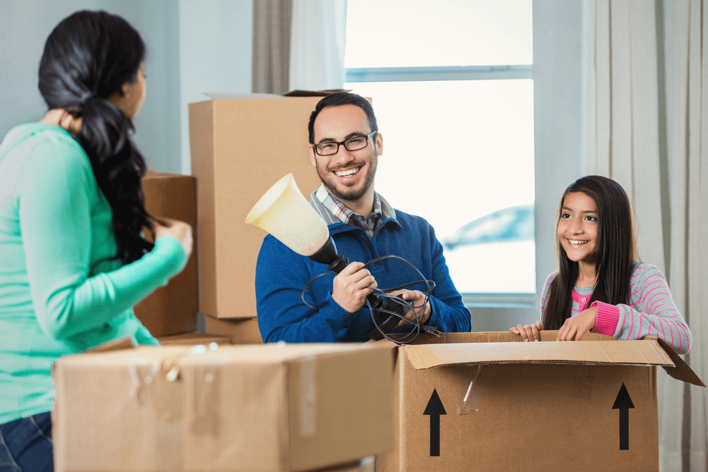 Father holding a lamp as daughter and mother help pack house moving boxes.