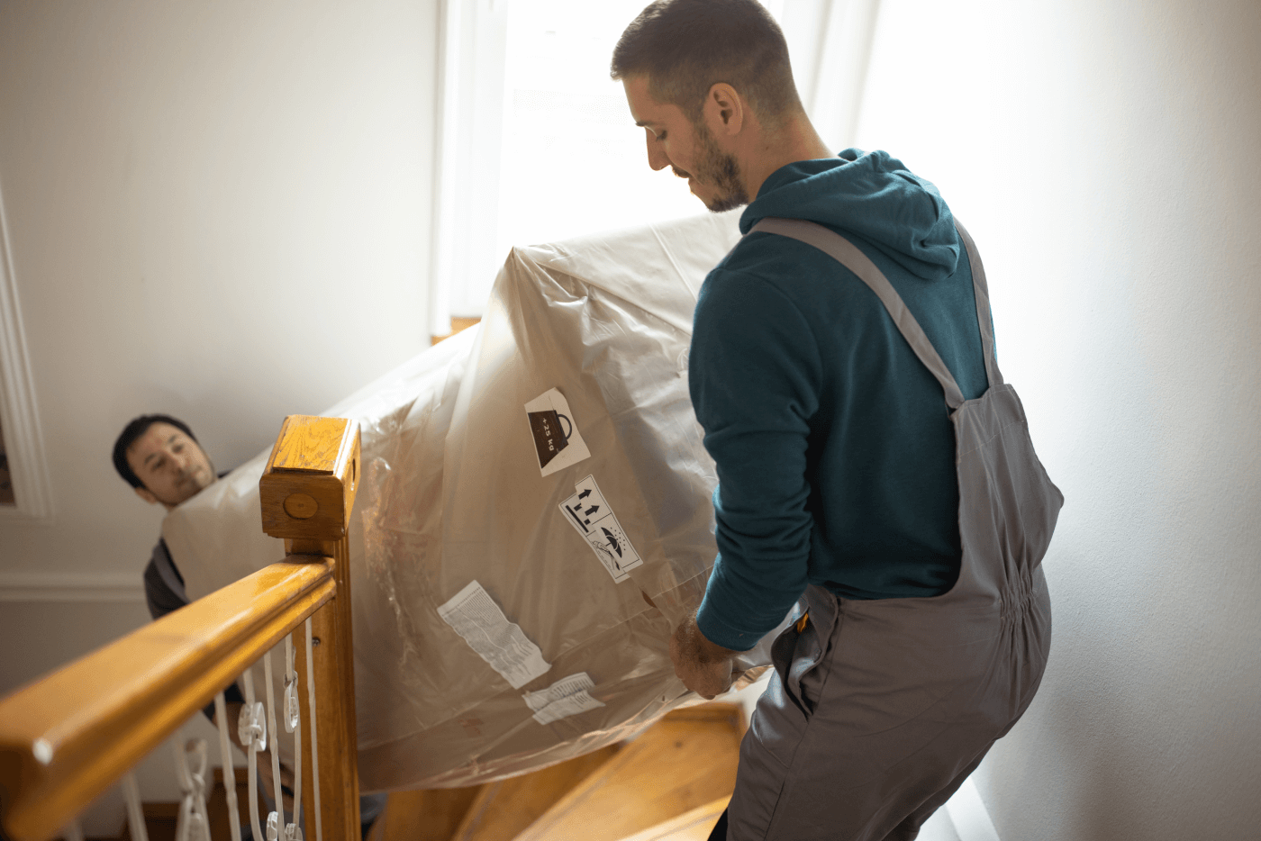 Two moving company employees moving a couch up a home stairs.