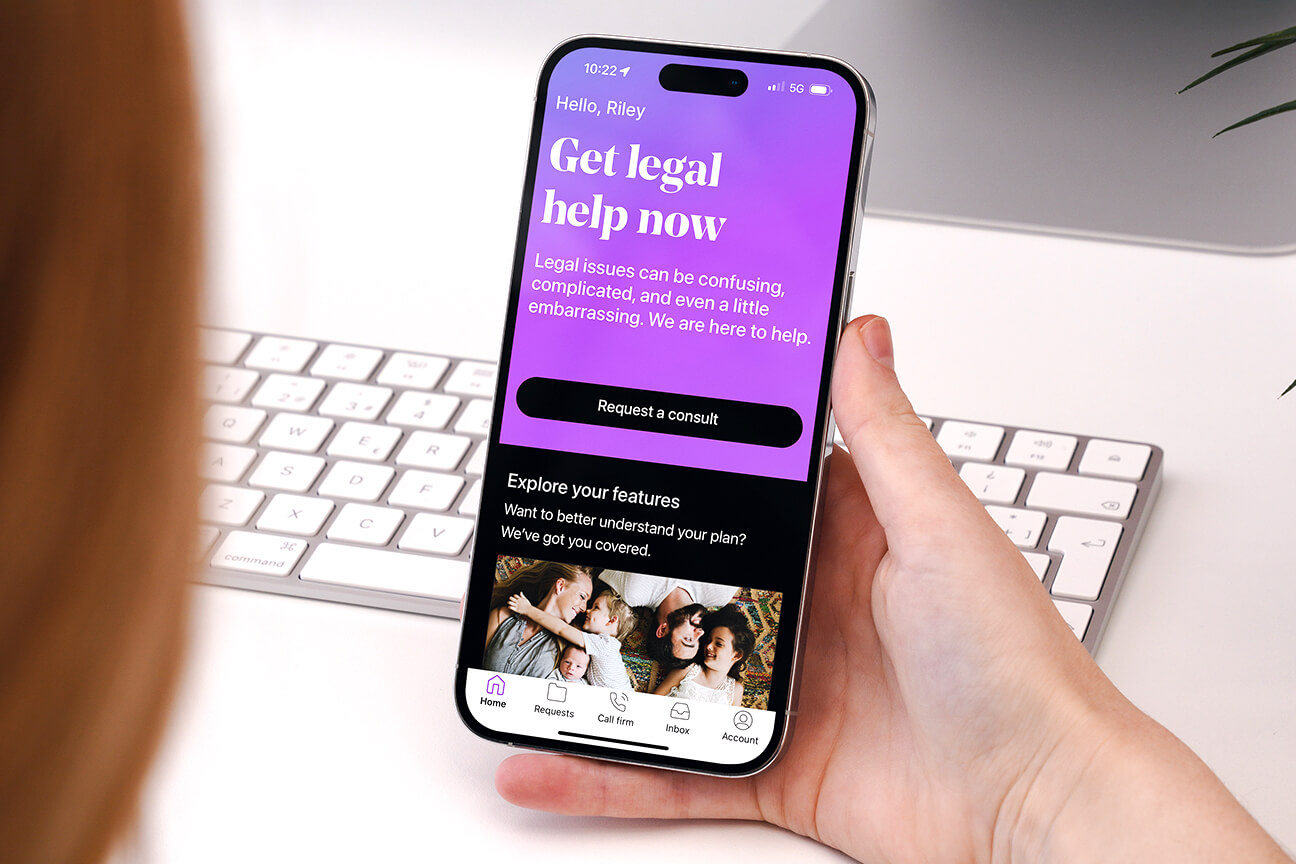 LegalShield app showing on a woman's phone screen as she sits in front of a keyboard.