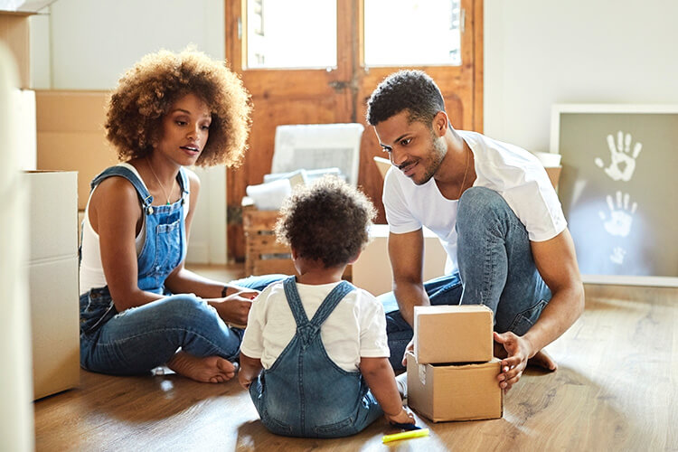 Mother, father and young toddler son on floor unpacking moving boxes.