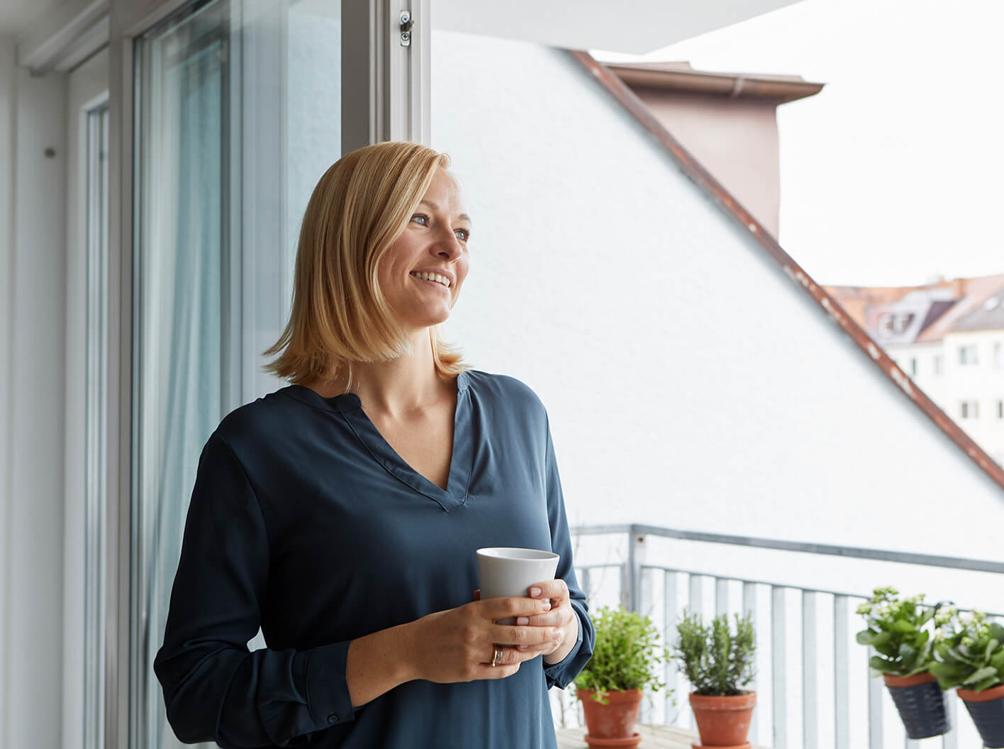 Smiling woman looking outside while holding a beverage mug.