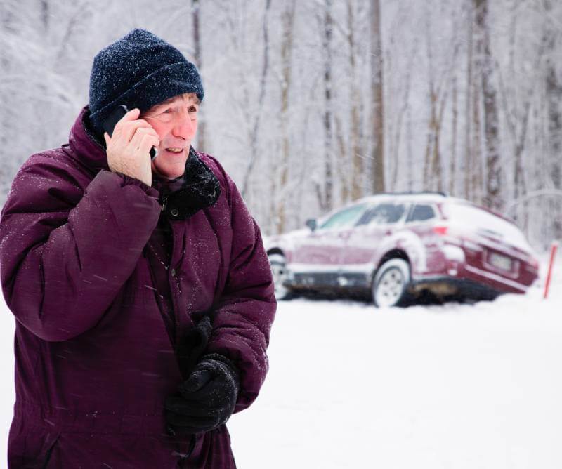 Man talking on his phone next to a car crash in the winter.