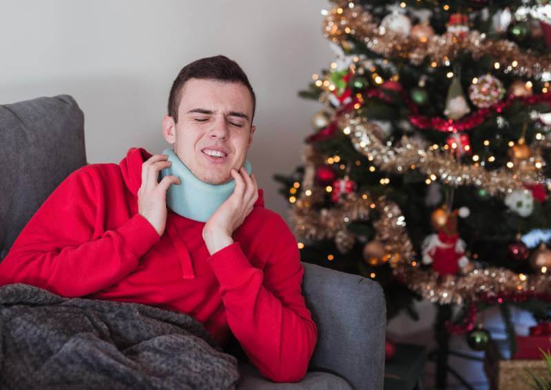 Young man wearing a neck brace sitting on a sofa next to a Christmas tree.